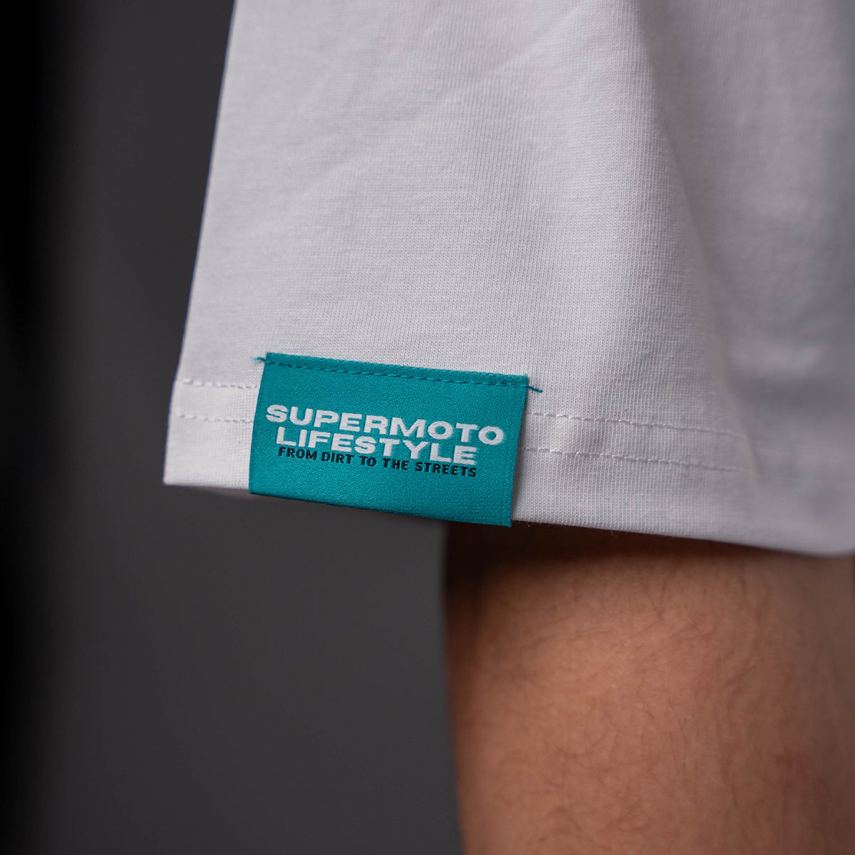 Close-up of teal 'Supermoto Lifestyle' tag on EWK Signature T-shirt sleeve