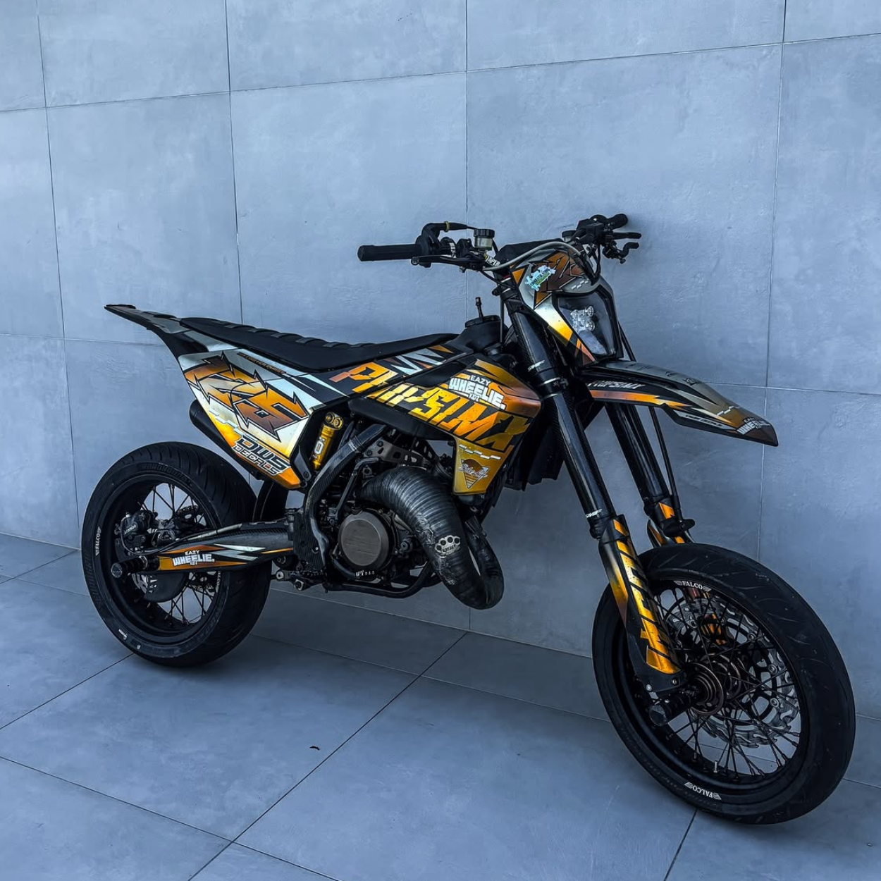 husqvarna te125 supermoto dirtbike with a full custom EazyWheelieKidz graphics kit standing against a wall